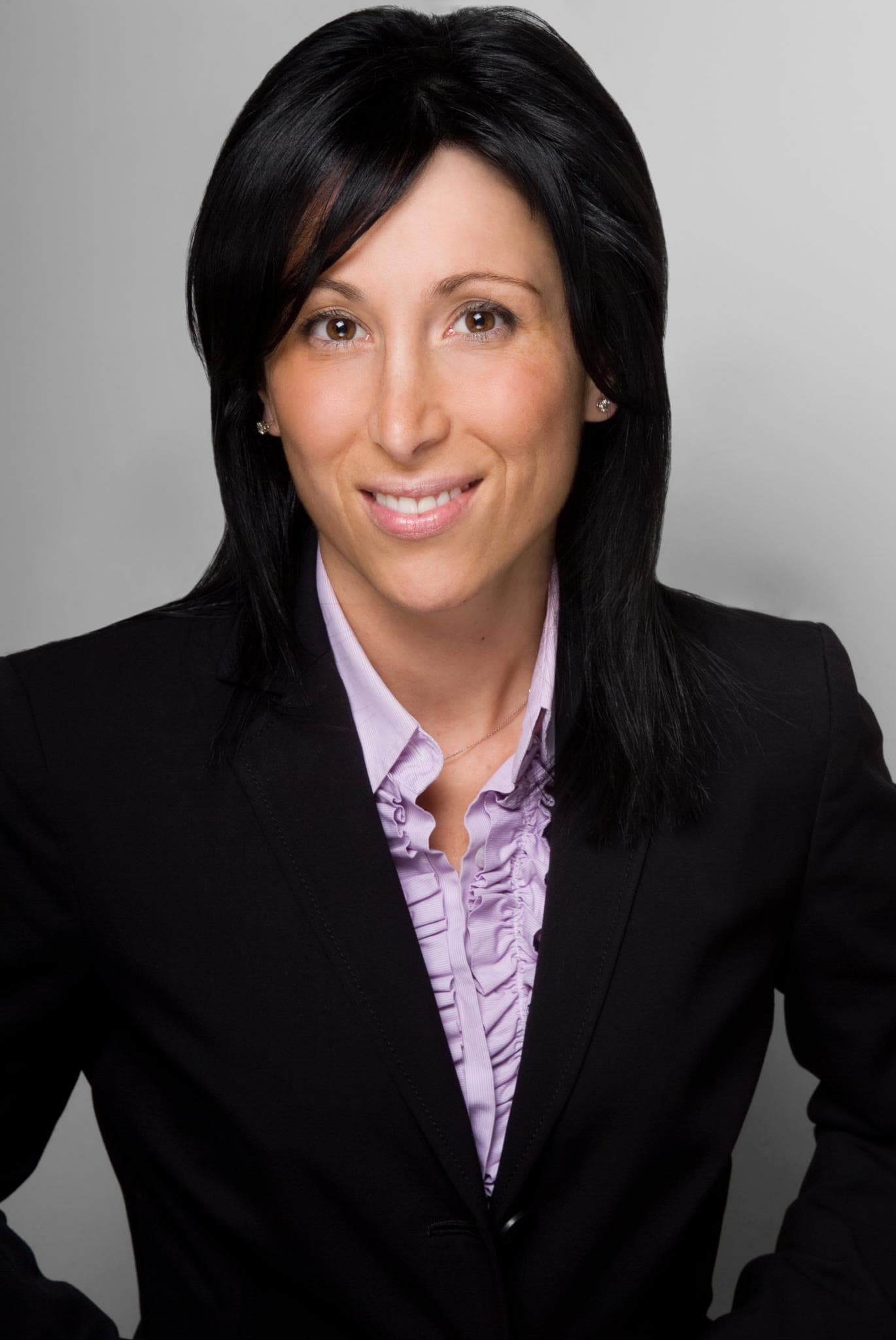 Professional headshot of a smiling woman with black hair wearing a blazer and ruffled shirt.